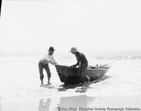 Two fishermen pulling rowboat on to beach
