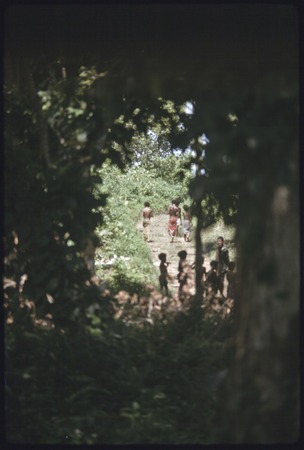 Children on the road out of the village, seen through a gap in the trees.