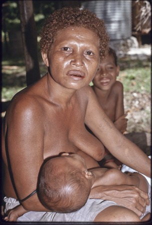 Woman holds sleeping baby, smiling child in background