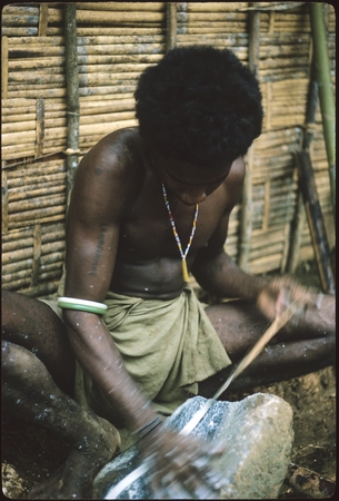 Man grinding shell money beads strung on special fiber.