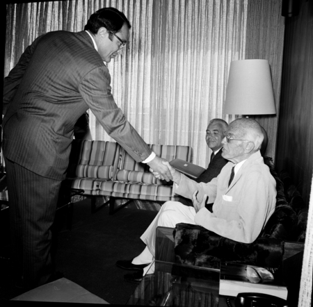 Ernest W. Mandeville (seated) shaking hands with unidentified man, with Chancellor William J. McGill (seated behind)