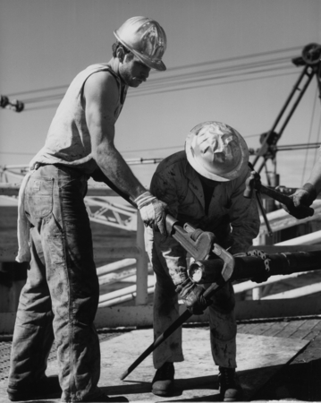 Derrickman Bob Kingsbury with a large wrench adding a pipe to the bottom hole assembly of one of the drilling pipes aboard...