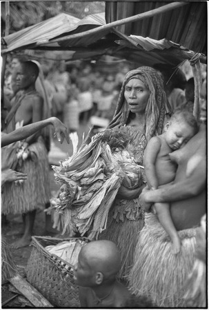 Mortuary ceremony, Omarakana: mourning woman holds large pile of banana leaf bundles at ritual exchange