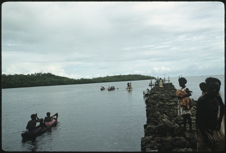 People at sea in canoes, and on rocky pier