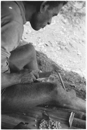Man chipping shell money beads with blade.