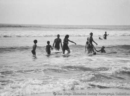 Children and adults wading in ocean surf at San Diego beach