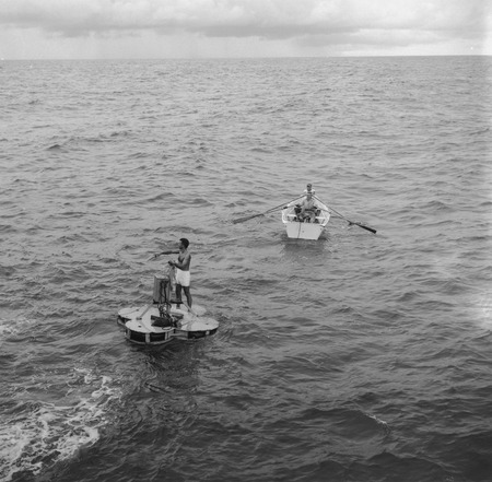 Willard Bascom on raft works on an oceanographic instrument, with John D. Isaacs and unidentified man in skiff, near Bikin...