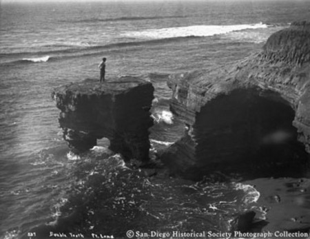 [Boy standing on top of Double Tooth rock formation in ocean surf at Point Loma]