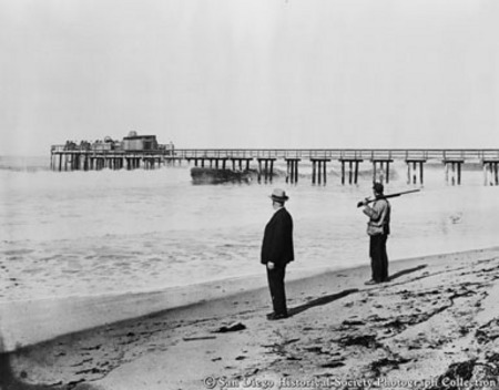 Two men on beach looking at Charles Ernest Edwards&#39;s wave motor on pier at Imperial Beach