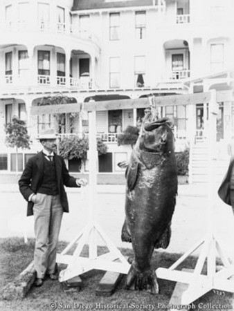 Man posing with giant bass on display outside Hotel del Coronado