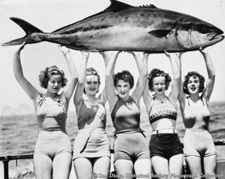 Five young women in bathing suits holding giant yellowtail tuna over their heads