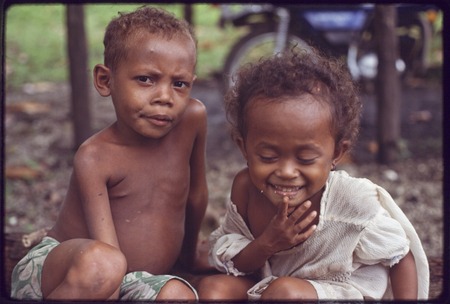 Children sitting on a log, Imala (r) smiles, boy (l) gazes at the photographer