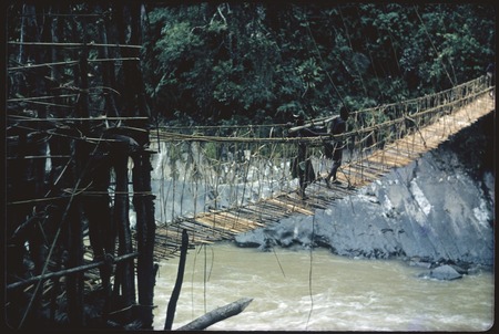 Jimi River area, men carry cargo across a narrow cane suspension bridge on way from Tabibuga to Kwiop