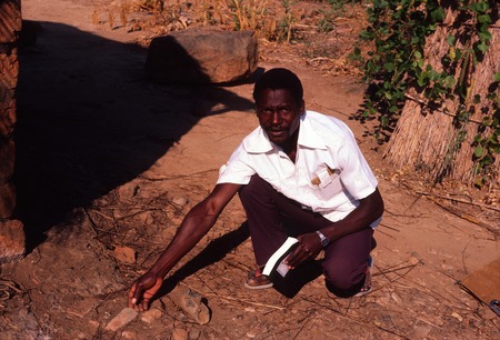 Man indicating remains of old iron working oven, Sumbu, Northern Province