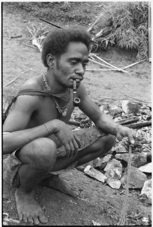 Man kneeling on ground with hand full of kofu shell money.