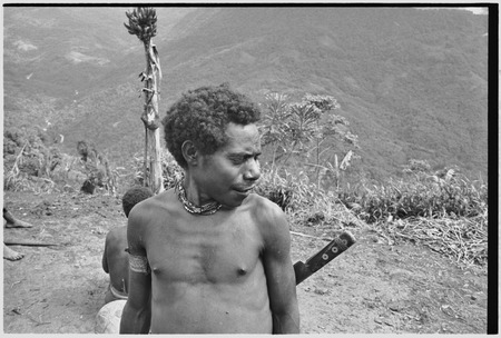 Man with woven armband, bead necklace and machete