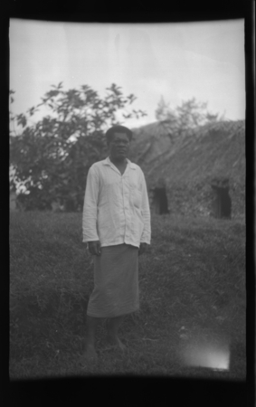 Fijian man in front of a traditional house
