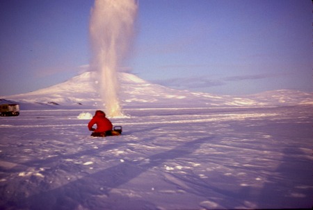 Dynamite blasting a hole through thick sea ice for scuba diving. Mount Erebus on Ross Island in background. during Paul Da...