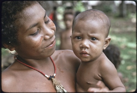 Adolescent girl, wearing shell necklace and dashes of betel nut paste on her cheeks, holding a baby