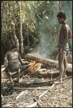 Two men heating log to remove bark.
