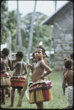 Dance: children wear colorful fiber skirts and carry pandanus leaves, girl (center) wears paint on face