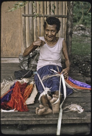 Weaving: smiling woman attaches dyed banana fibers to a cord wrapped around her foot, creating a colorful skirt