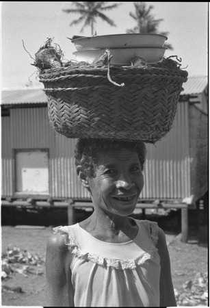 Smiling older woman with basket of food and bowls carried on her head