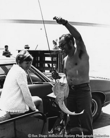 Striking longshoreman showing catch [of small shark?] to woman