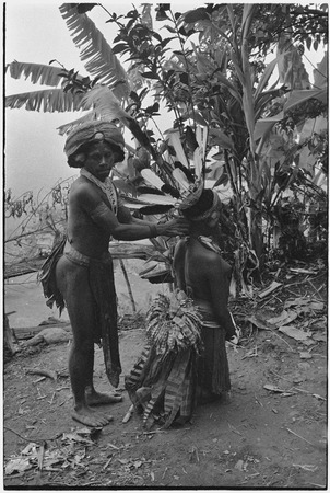 Pig festival, stake-planting, Tuguma: man adjusts headdress worn by unmarried woman