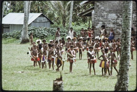 Dance: children wear colorful fiber skirts and carry pandanus leaves, line up for circle dance near church building