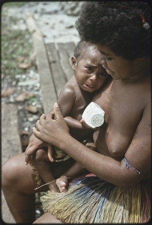 Woman comforts crying baby, who holds medicine bottle