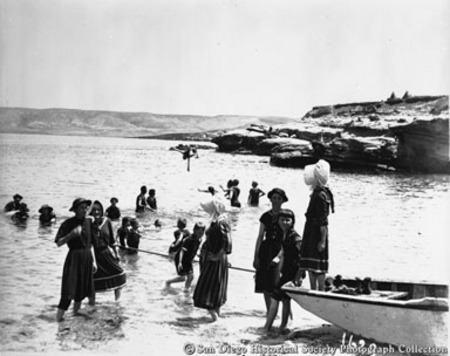 People wading in ocean, standing by rowboat, La Jolla beach