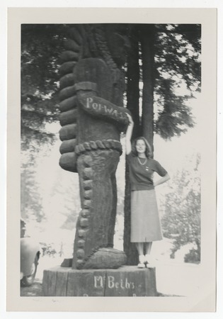 Woman posing with an unidentified large wooden carving of an American Indian