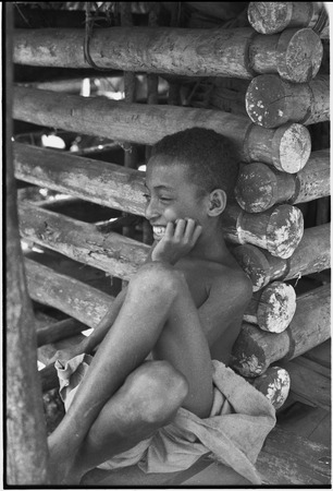 Boy leans against wall of a yam house, with good detail of notched pole construction