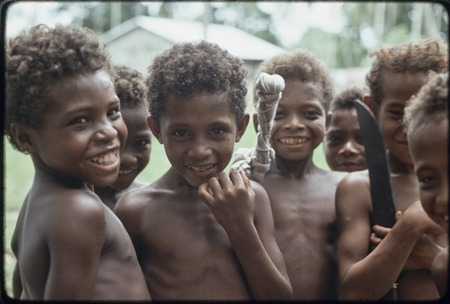 Boys smiling, one holding something with cloth twisted around it, another boy holds a machete