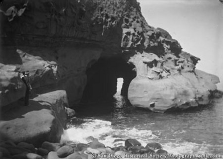Two men standing on rock formation looking at White Lady Cave, La Jolla