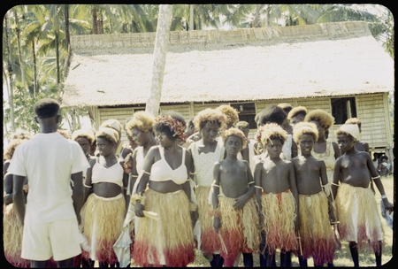 Group of dancers in grass skirts and matching headress; some with western dress or tops