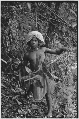 Hunting: Akis, wearing a barkcloth cap, cuts materials for a snare