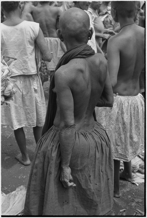 Mortuary ceremony: mourning woman with shaved head at ritual exchange of banana leaf bundles