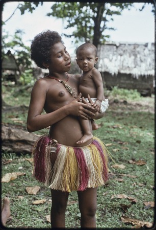 Adolescent girl, wearing short fiber skirt and shell necklace, dabs of betel nut paste on face, holding a baby