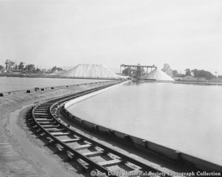 Railroad track running across seawater reservoirs toward salt mounds and processing facility, Western Salt Company