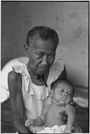 Elderly woman, Bomtavau, holding young infant, perhaps her grandchild