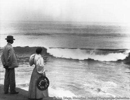 Man and woman standing on rock watching ocean waves, La Jolla
