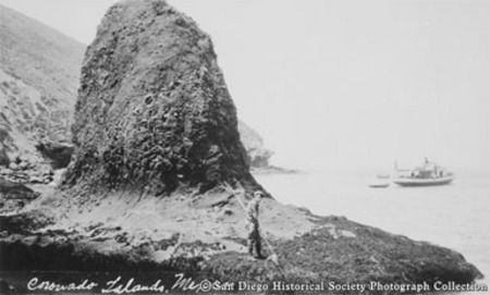 [Man spear fishing near large rock formation on Coronado islands]