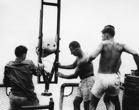 Robert Floyd Dill, Walter Heinrich Munk, and Richard Blumberg prepare to lower a deep-sea camera enclosed in a watertight ...