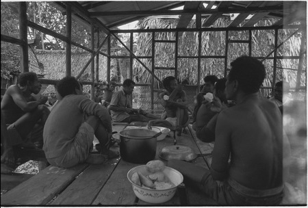 House-building: men share meal of yams in building under construction