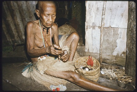 Bomtavau, her head shaved as a sign of mourning, uses a mortar and pestle to prepare betel nut (areca)