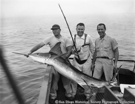 Three men at stern of fishing boat posing with swordfish