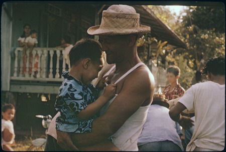 Local man wearing handwoven hat, holding child, on Moorea