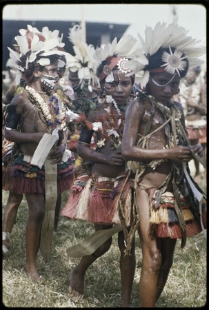 Dance: children wear short grass skirts, shell necklaces, and feather headdresses, carry flattened pandanus leaves